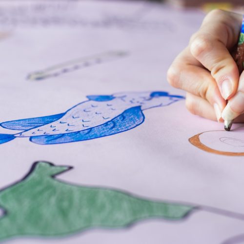 detailed view of the hand of a young college girl, painting with her brown pencil, a handmade drawing on a pink cardboard. doing homework at home before going to school. college concept.