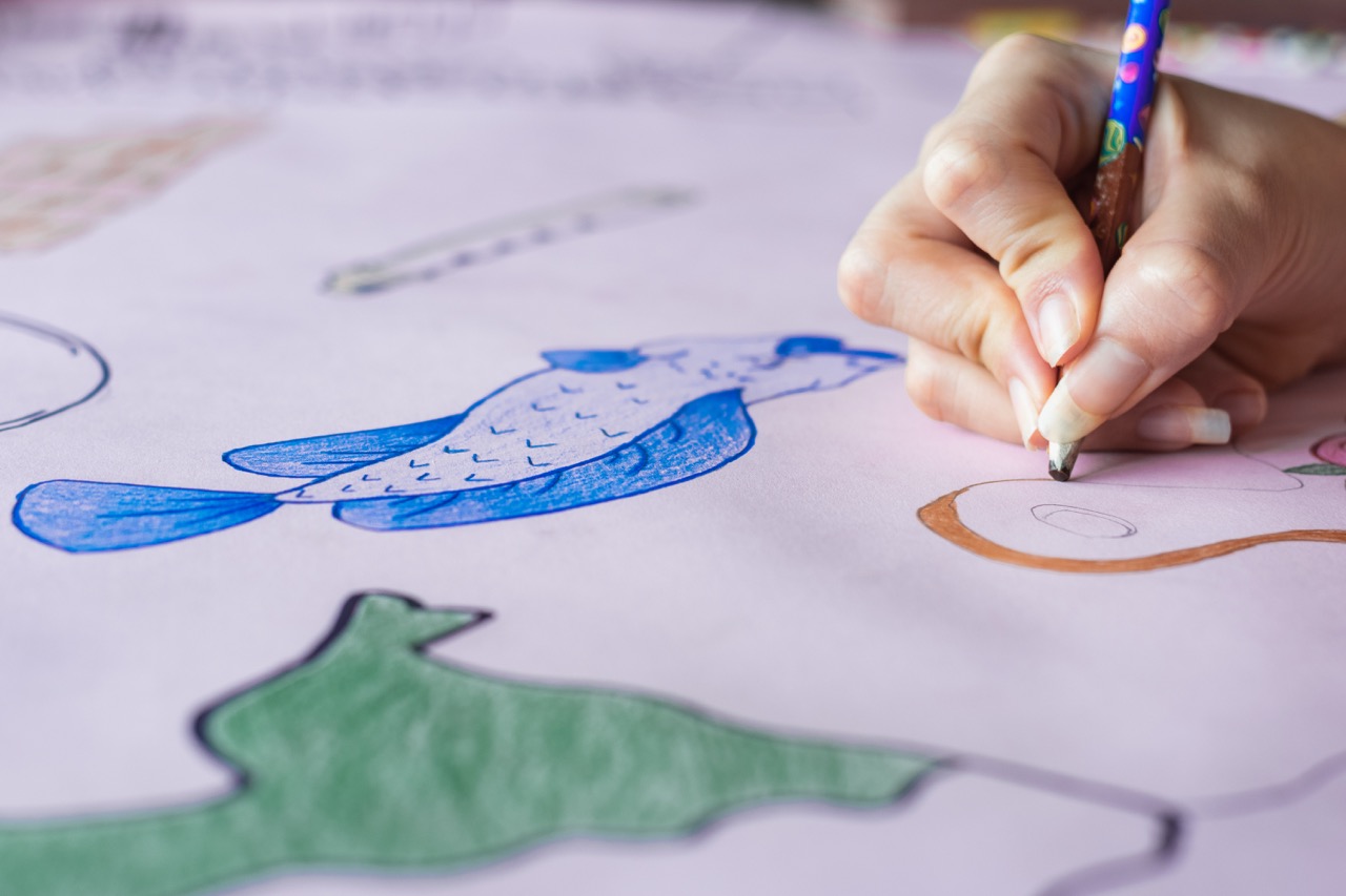 detailed view of the hand of a young college girl, painting with her brown pencil, a handmade drawing on a pink cardboard. doing homework at home before going to school. college concept.